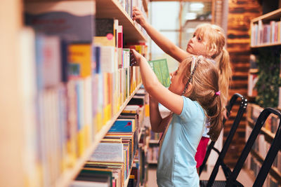 Schoolgirls looking for books in school library. students choosing set books. back to school