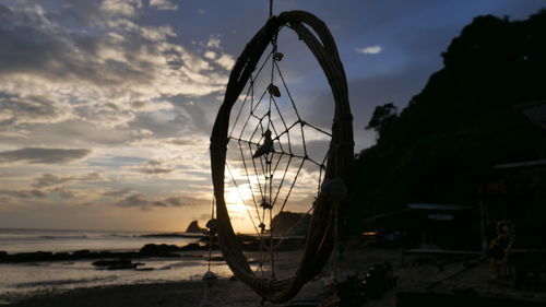 Silhouette ferris wheel on beach against sky at sunset