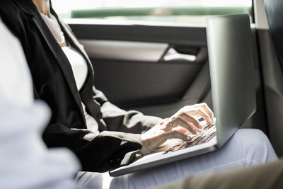 Midsection of businesswoman using laptop in taxi