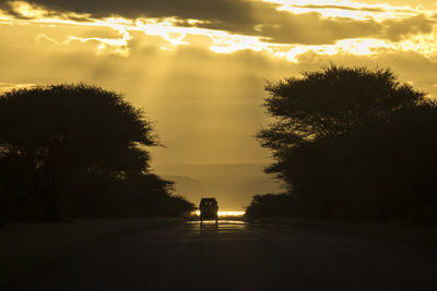 Silhouette people on road against sky during sunset