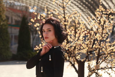 Portrait of young woman standing by plant at park