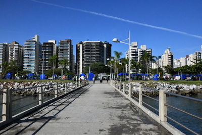 Road by canal and buildings against blue sky