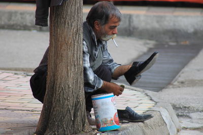 Side view of woman using mobile phone while sitting on footpath