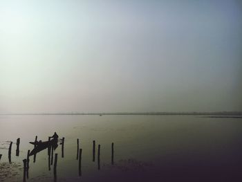 Silhouette of wooden posts in lake against sky