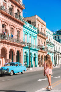 Rear view of girl standing on street against buildings in city