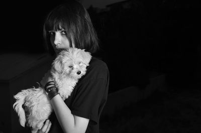 Portrait of woman holding puppy against black background