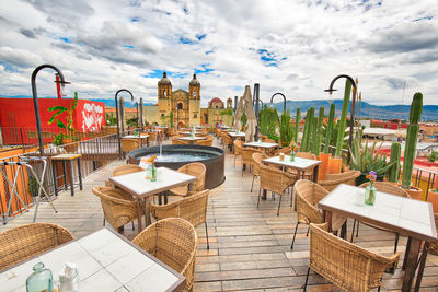 Empty chairs and tables at sidewalk cafe against sky