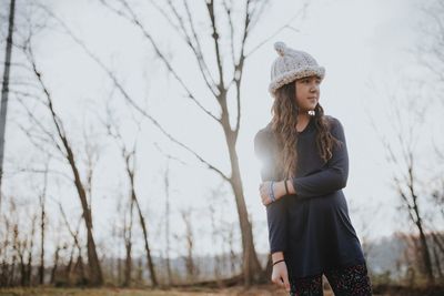 Girl looking away while standing against bare trees