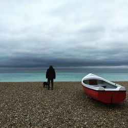 Rear view of man overlooking calm sea against cloudy sky