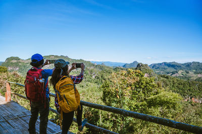 Rear view of people looking at mountain against blue sky