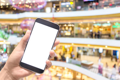 Cropped hand holding blank smart phone in illuminated mall