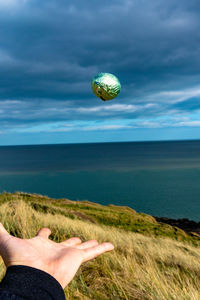 Midsection of person hand on sea shore against sky