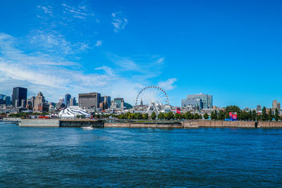 View of ferris wheel and cityscape against blue sky