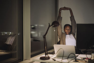 Tired businesswoman stretching hands while working in office at night