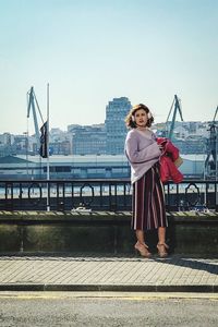 Portrait of young woman standing on railing against cityscape