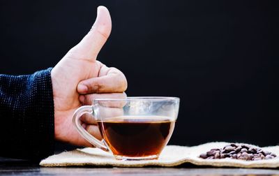 Cropped image of hand holding coffee cup against black background