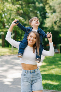 Beautiful young woman in denim clothes plays with her little son in the park in the summer