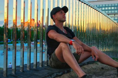 Young man looking away while sitting on fence