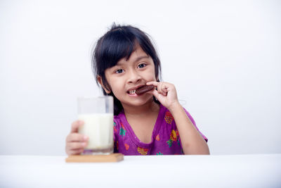 Young woman using mobile phone while sitting on table against white background