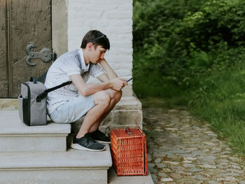 One guy with a picnic basket sits on the steps and looks through the news feed on his smartphone