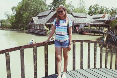 Portrait of mid adult woman standing on footbridge over lake during sunny day