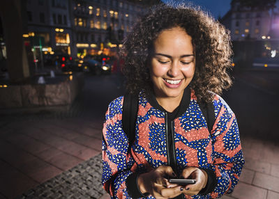 Smiling young woman using smart phone in city