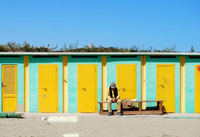 Man sitting on bench against beach huts