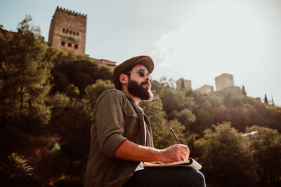 Man writing in book while sitting outdoors