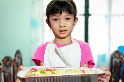 Portrait of cute girl holding food in tray at home