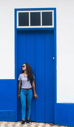 Woman wearing sunglasses standing against blue wall outdoors