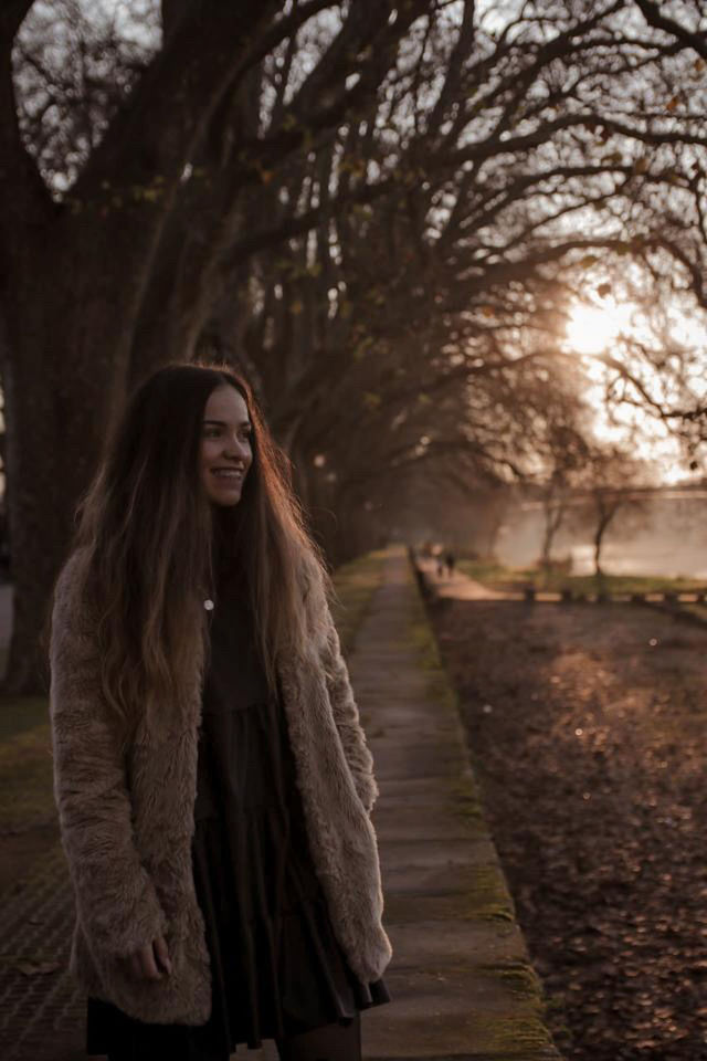 PORTRAIT OF SMILING WOMAN STANDING AGAINST TREES