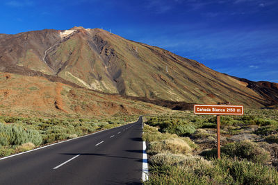 Empty road along rocky landscape against blue sky