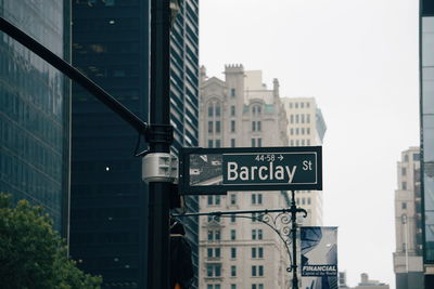 Road sign by buildings against sky in city