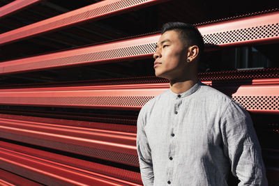 Man looking away while standing against metal wall