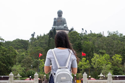 Rear view of woman standing by trees against clear sky