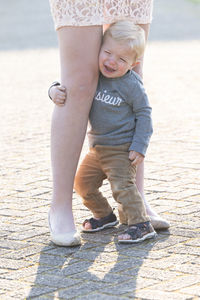 Sad caucasian blonde little boy hugging her mother legs