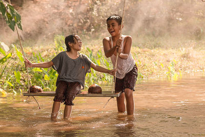 Happy boy standing by sister on swing in pond