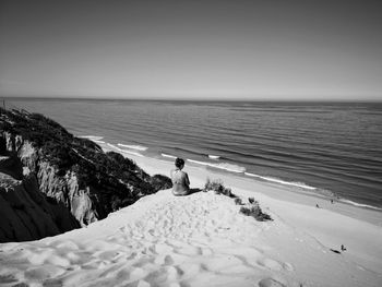 Rear view of woman sitting at beach against clear sky