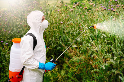 Man in protective suit and mask spraying herbicide on weed