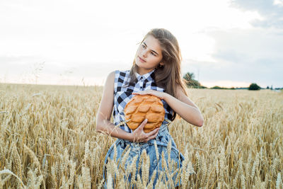 Teenager girl holding loaf of bread while standing amidst farm