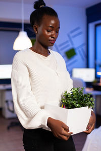 Young woman looking away while standing on potted plant