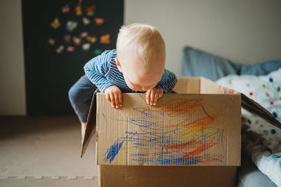 Young toddler playing and drawing in a box at home during lockdown