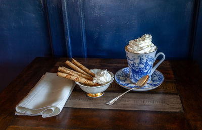 Gourmet hot chocolate and whip cream in a nautical china mug with cookies on a rustic table