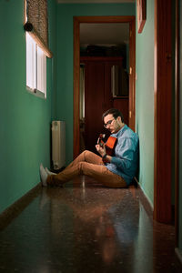 Young man plays guitar sitting in the hallway of his house
