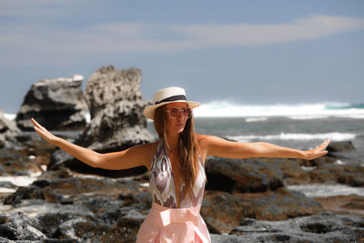 Woman wearing hat on rock at beach against sky