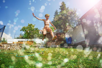 Rear view of woman with arms raised standing on field against sky