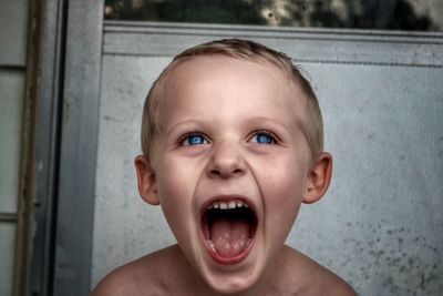 Close-up of shirtless boy with blue eyes screaming outdoors