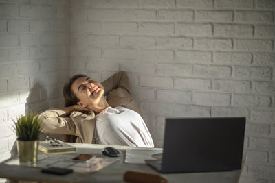 Smiling young manager sitting at the table stretching her back, arms. work-life-balance, copy space