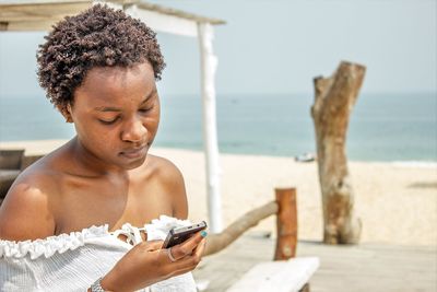 Close-up of woman holding smart phone at beach against sky