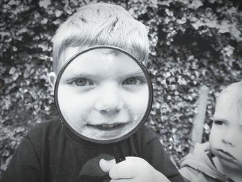 Portrait of boy looking through magnifying glass while standing with sibling